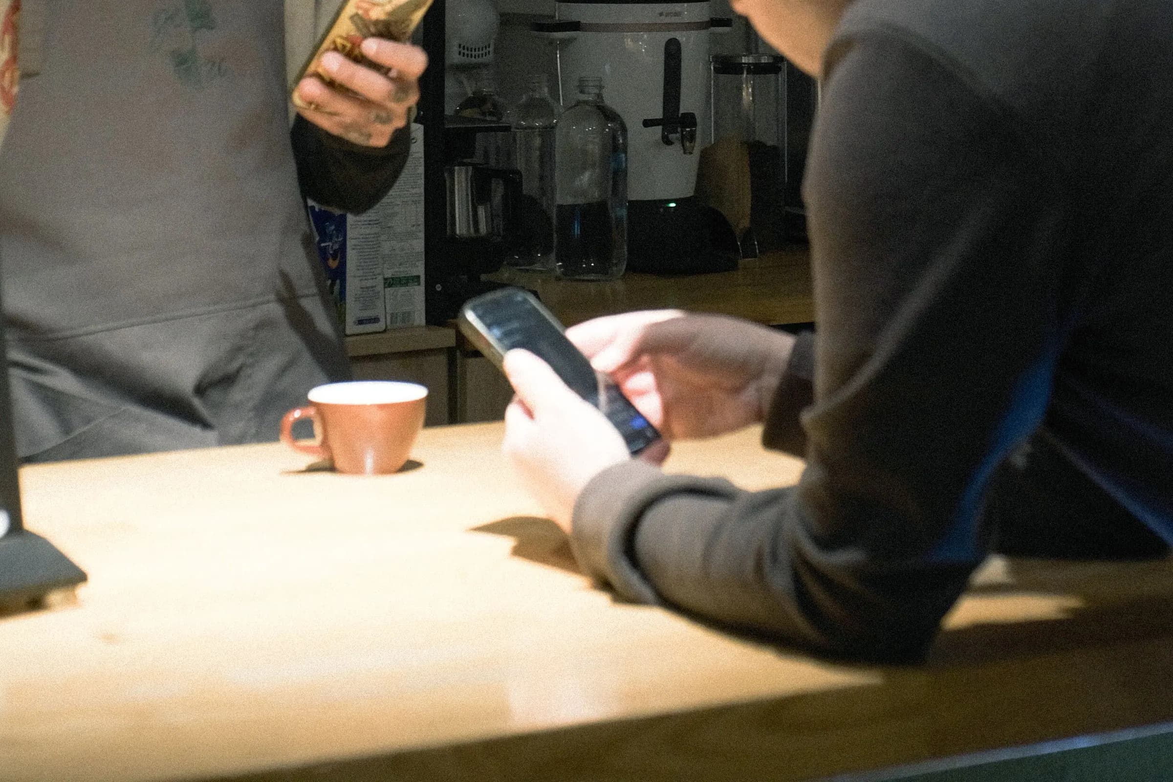 Customer using a smartphone while speaking with staff at a cafe counter