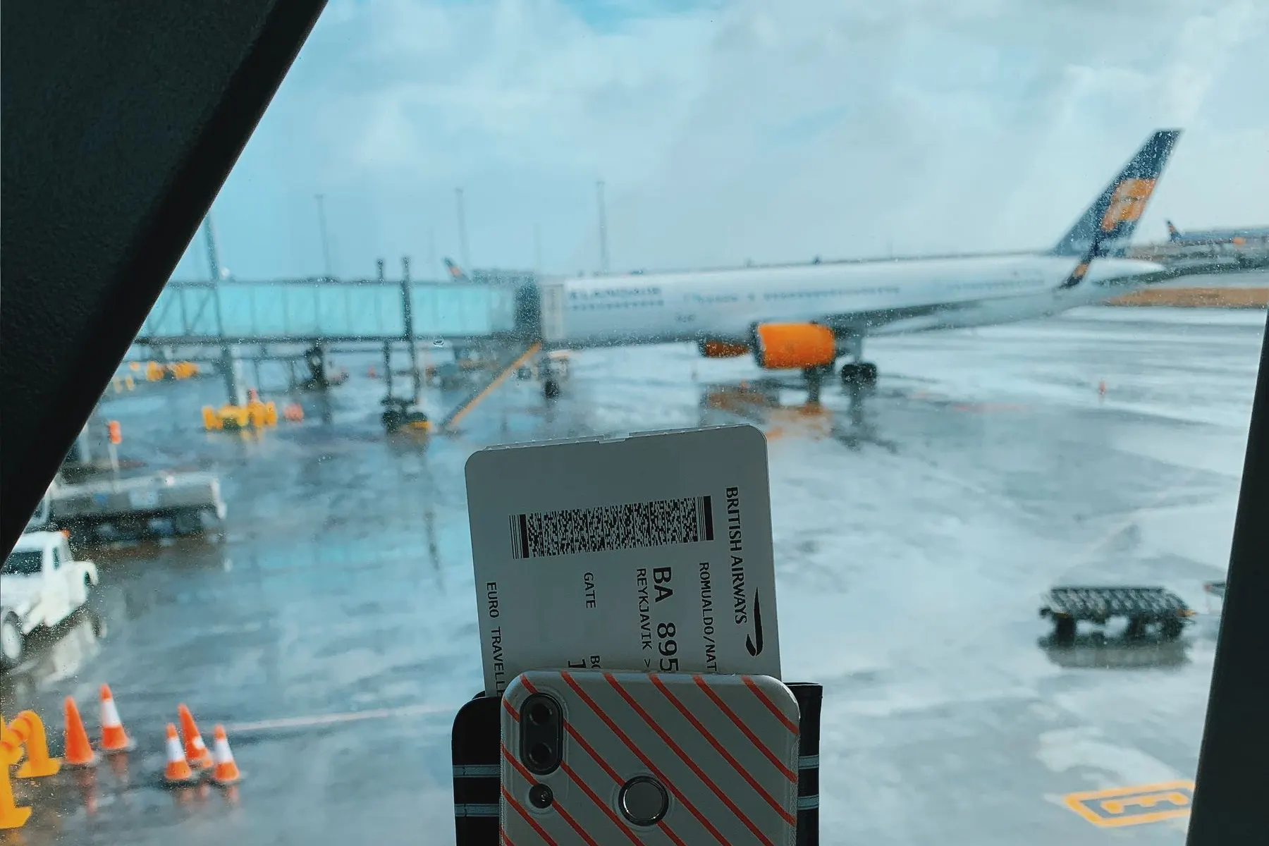 Traveler holding a smartphone and boarding pass beside an airport window