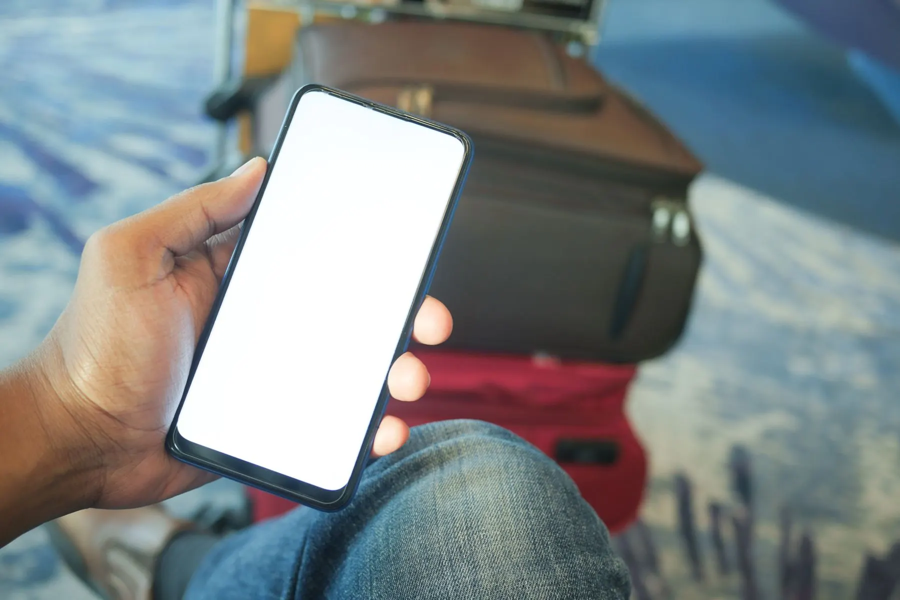 Traveler checking a smartphone beside airport luggage