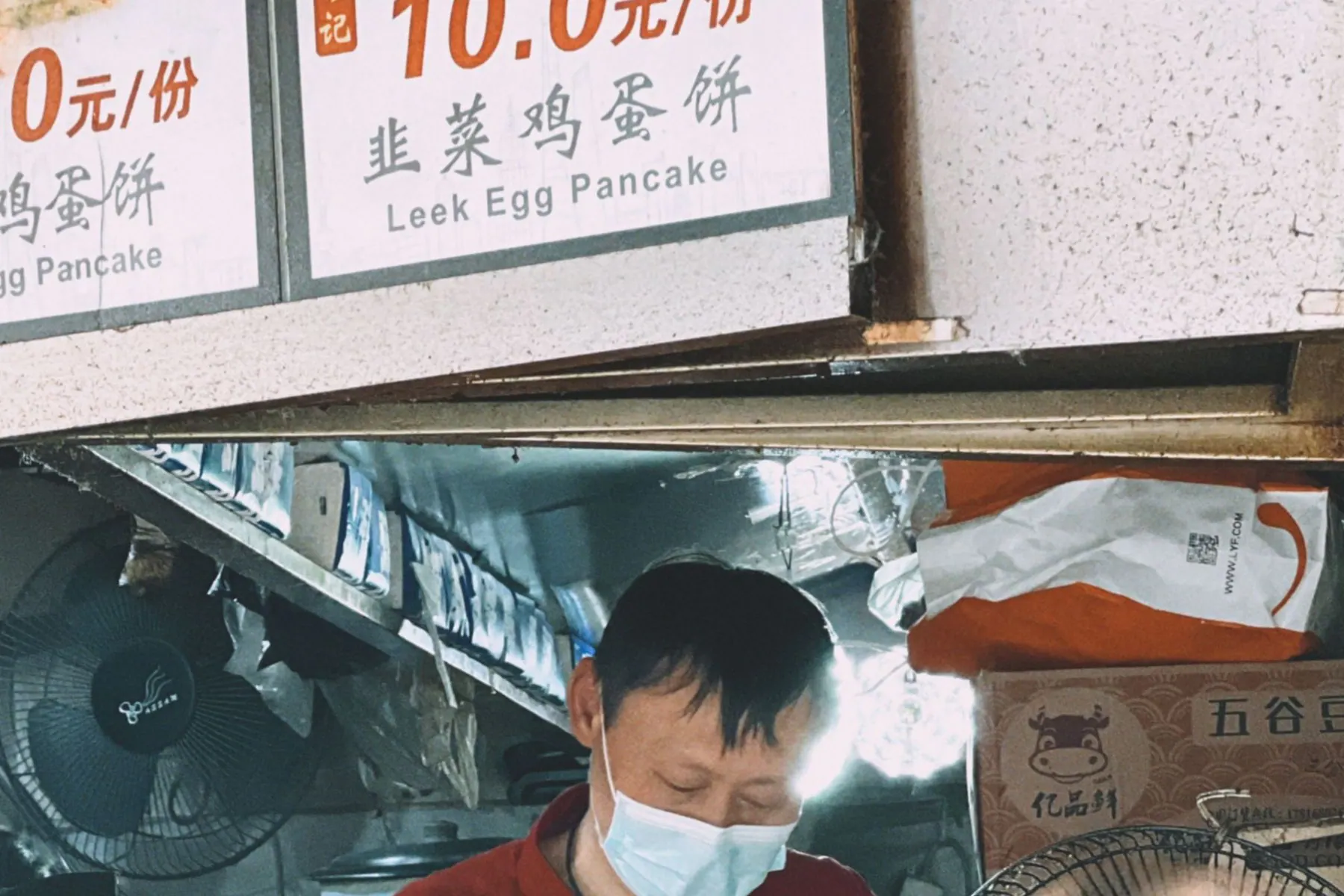 Chinese street-food cook working beneath a visible menu