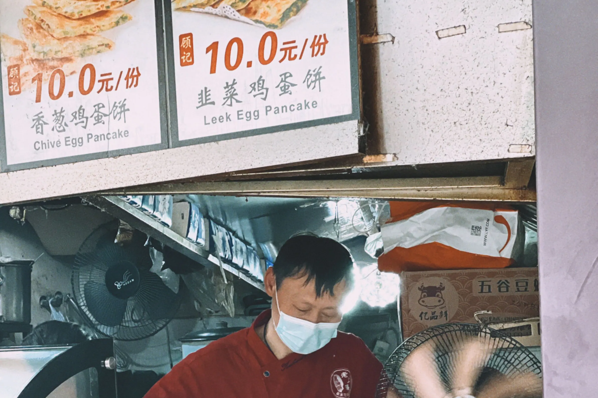 Cook preparing food beneath Chinese menu signs at a Shanghai street stall